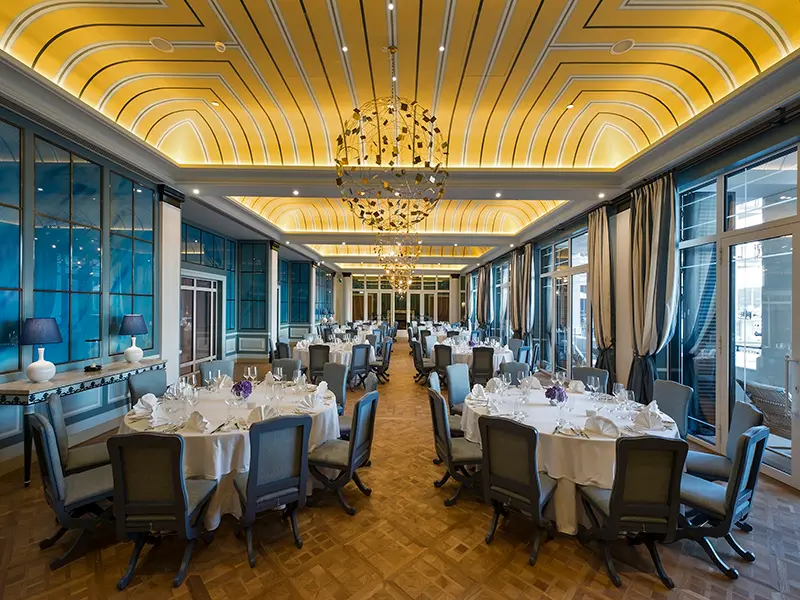 Balna sala u Regent Porto Montenegro sa okruglim stolovima za banket, sivim stolicama, belim stolnjacima, zlatnim art deco plafonom i lusterom