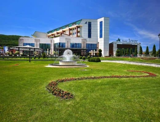 Spoljašnjost Hotel Izvor sa fontanom, zelenim travnjakom, cvećem i natpisom na fasadi