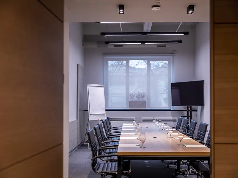 Boardroom sala u Hotel Mona Plaza sa drvenim stolom, crnim kožnim stolicama, TV ekranom i flipčartom