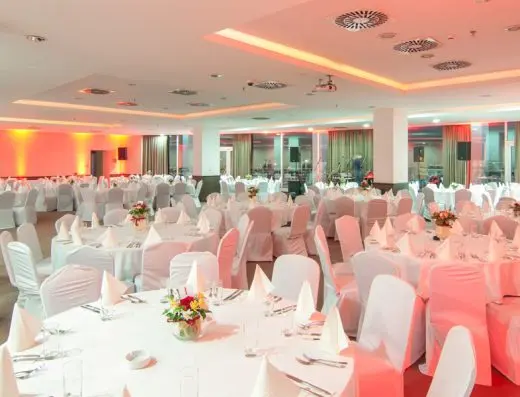 Banket sala u Hotel Ramada Podgorica pripremljena za svečanost sa belim stolovima, ružičastim ambijentalnim osvetljenjem i cvetnim aranžmanima