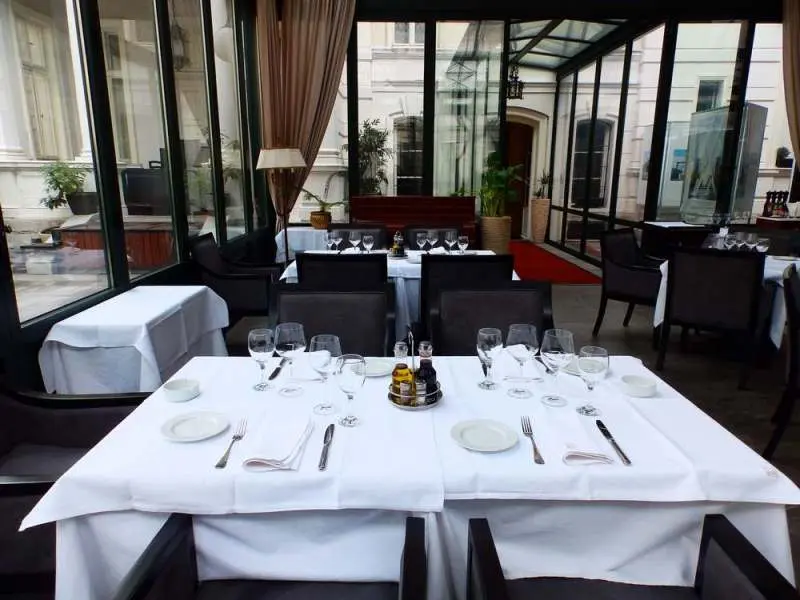 Detalj stola u zimskoj bašti Restorana Klub književnika sa tamnim foteljama i pogledom na fasadu