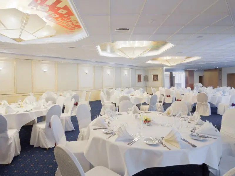 Banket sala u Crowne Plaza Bucharest Hotel sa okruglim stolovima, belim stolnjacima, belim navlakama za stolice, elegantnom postavkom i osvetljenim plafonom