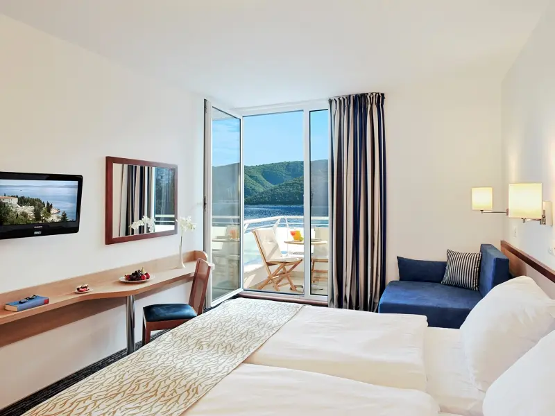 Soba u Valamar Sanfior Hotel sa belim krevetom, plavom foteljom, radnim stolom, TV-om i balkonom sa pogledom na more i planine