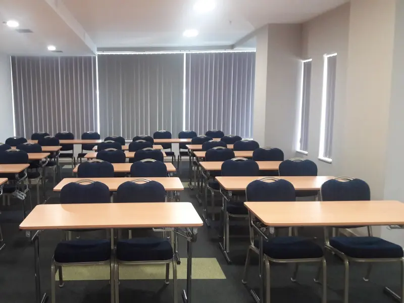 Konferencijska sala u Tre Canne hotelu sa stolovima u učioničkom rasporedu, plavim stolicama i vertikalnim roletama