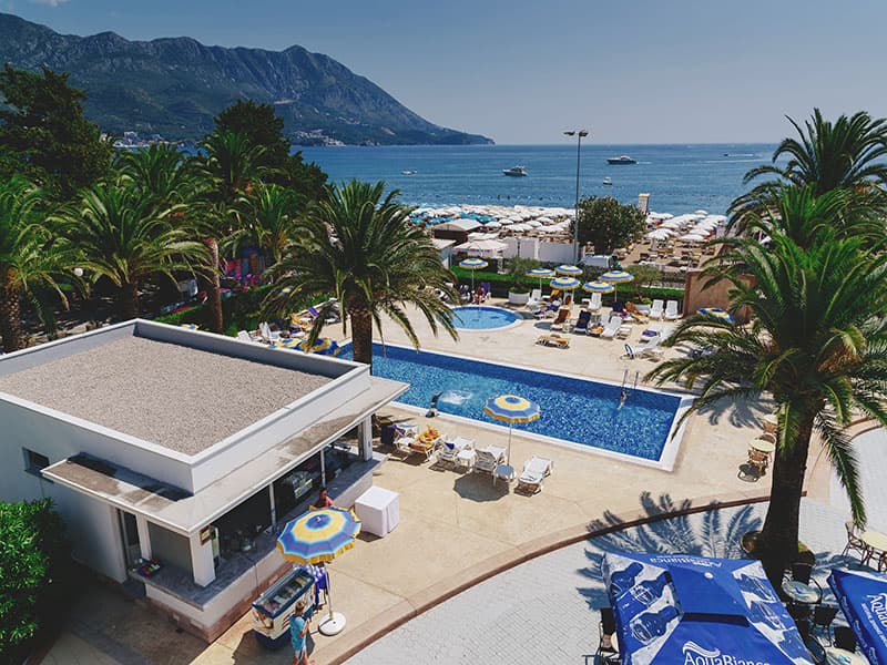Spoljni bazen Hotel Montenegro sa pool barom, palmama, pogledom na plažu, more i planine u pozadini