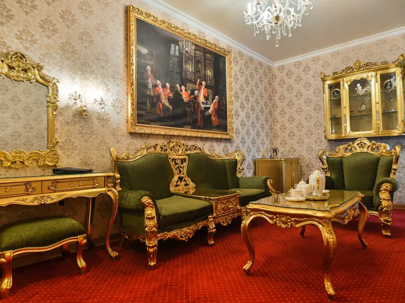 Apartman u Prezident Palace Belgrade sa zelenim baroknim foteljama u zlatnom okviru, crvenim tepihom, kristalnim lusterom, zlatnim ogledalom i vitrinom