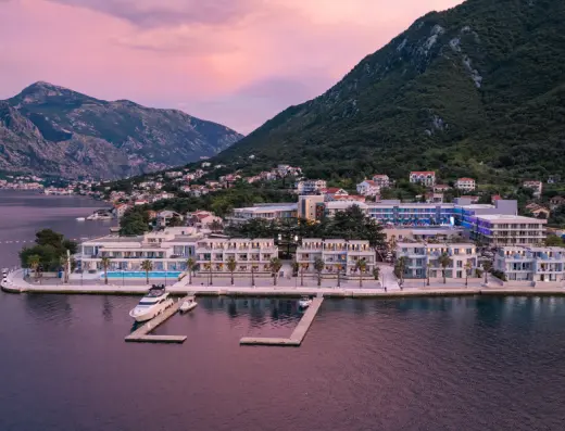 Panoramski pogled iz vazduha na Hyatt Regency Kotor Bay Resort u sumrak sa marinom, osvetljenom fasadom, planinama i Bokom Kotorskom