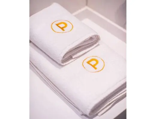 Detalj belih peškira u Premium Hotel sa zlatnim vezenim monogramom P u krugu