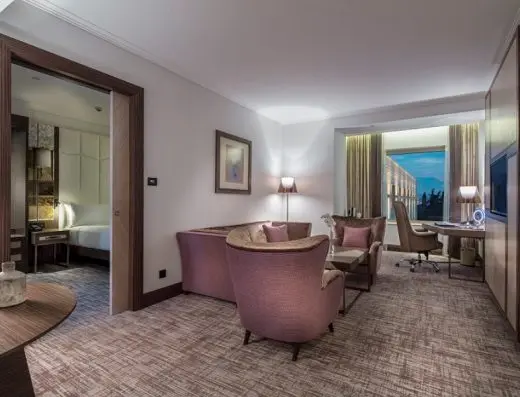 Dnevna soba apartmana u Hilton Podgorica Crna Gora hotelu sa ljubičastim foteljama, kaučem, radnim stolom i pogledom na spavaću sobu