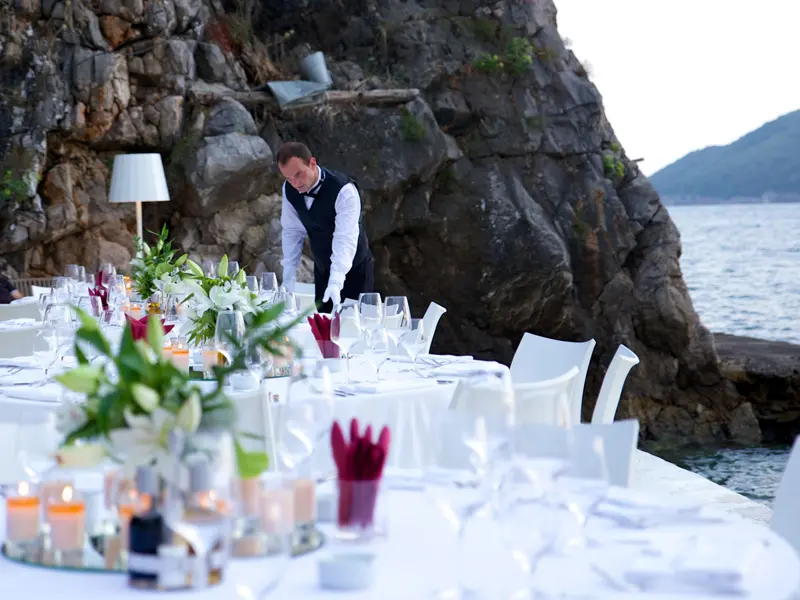 Elegantna večera u Key West Beach & Restaurant sa belim stolnjacima, cvećem i konobarom na obali uz stene