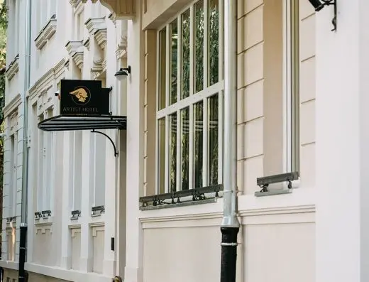 Spoljašnjost Artist Hotel Subotica sa crnom tablom sa zlatnim logoom, elegantnom belom fasadom i velikim prozorima