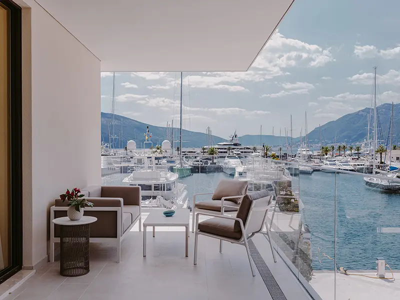 Balkon sobe u Regent Porto Montenegro sa elegantnim foteljama, belim stolićem i panoramskim pogledom na marinu sa luksuznim jahtama i planinama