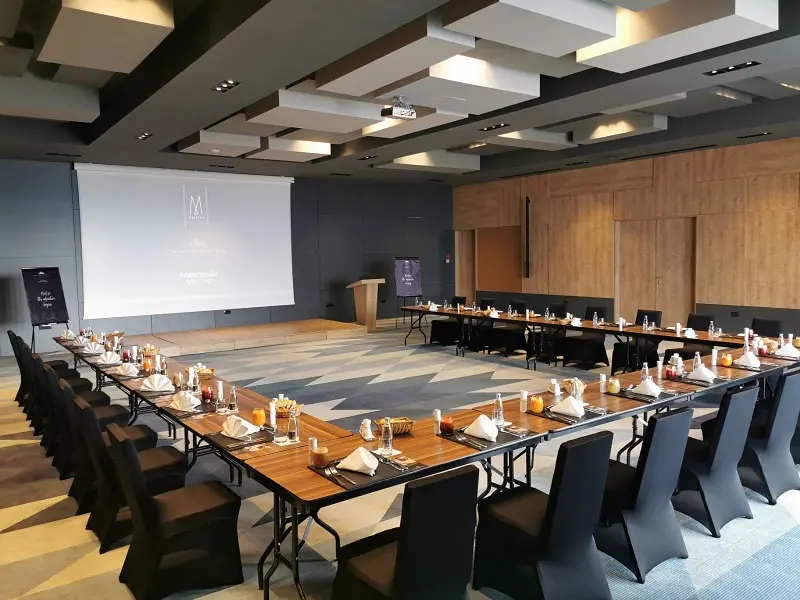 Konferencijska sala u Tarčin Forest Resort & Spa Sarajevo hotelu sa stolovima u U-rasporedu postavljenim za poslovni doručak, projekcijom i govorničkim pultom