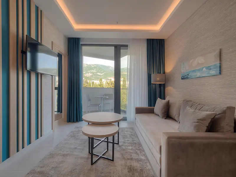 Dnevna soba apartmana u Hotel Montenegro sa kaučem, okruglim stolićima, TV-om i balkonom sa pogledom na brda