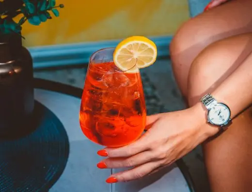 Detalj koktela Aperol Spritz na stočiću u baru Hotel voco Podgorica sa kriškikom limuna, žutim zidom u pozadini i elegantnom čašom