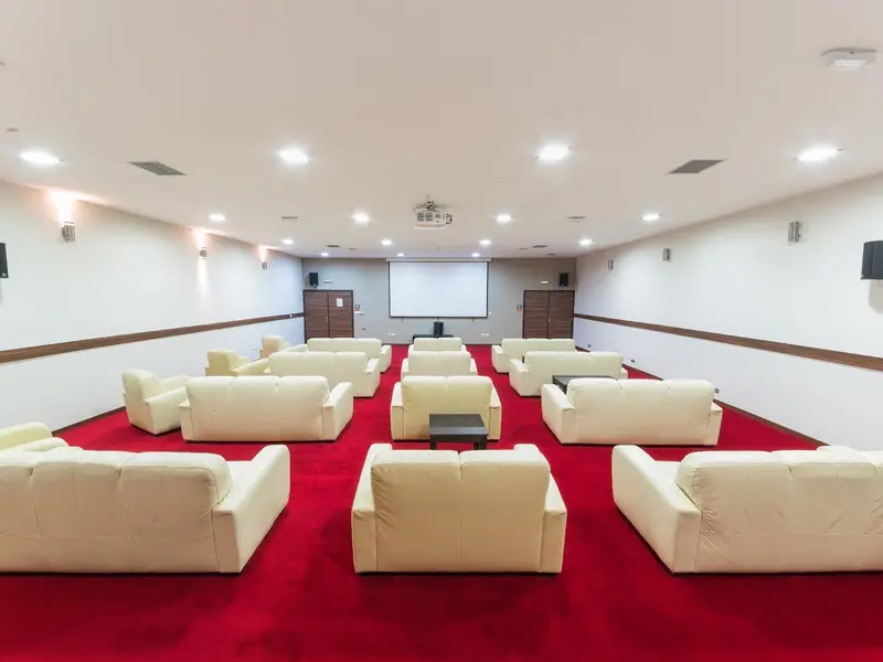 Bioskopska sala u Garden City Hotel Konjic & Resort sa belim kaučima i foteljama, projekcionim platnom, crvenim tepihom i zvučnicima