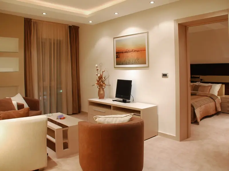 Apartman u Hotel Vojvodina sa dnevnim boravkom, braon kožnom foteljom, belim komodom, slikom zalaska sunca i pogledom na spavaću sobu