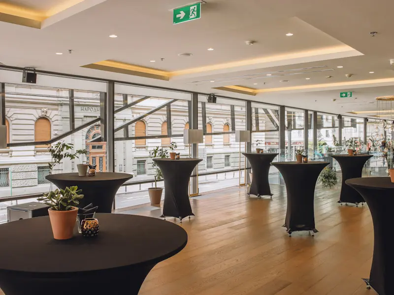 Event prostor u hotelu Courtyard Belgrade City Center sa visokim koktel stolovima u crnim navlakama, panoramskim prozorima, pogledom na grad i parketom