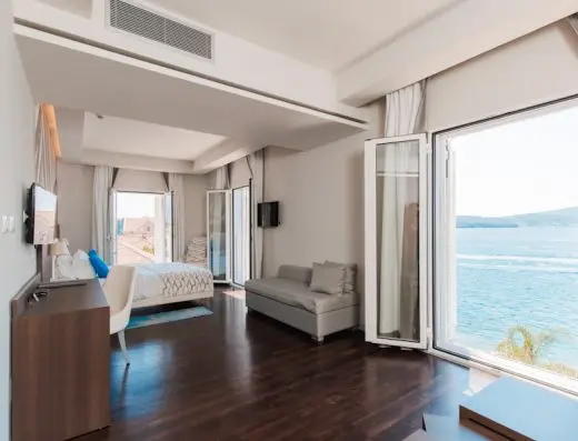 Suite soba u Hotel Palma sa bračnim krevetom, sivim kaučem, radnim stolom i panoramskim pogledom na more kroz otvorene prozore