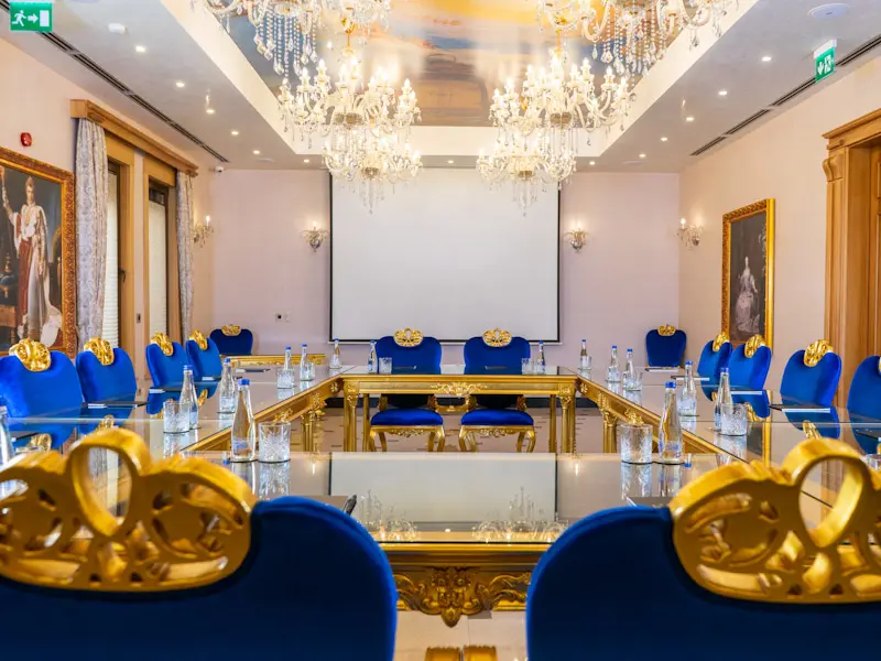 Konferencijska sala u Prezident Palace Belgrade sa stolovima u U-rasporedu, plavim stolicama, kristalnim lusterima, projekcionim platnom i plafonskom freskom