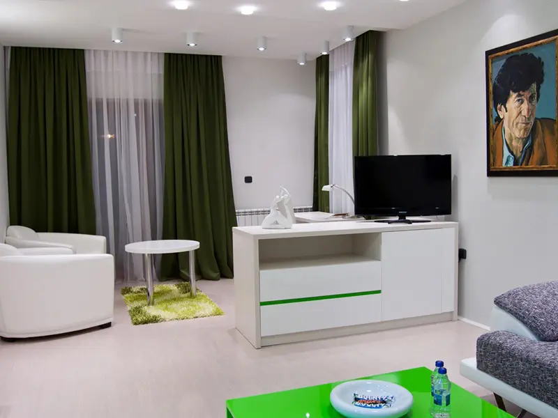 Dnevna soba apartmana u Hill Hotel sa zelenim zavesama, belim nameštajem, zelenim stolićem, belom foteljom i portretom na zidu