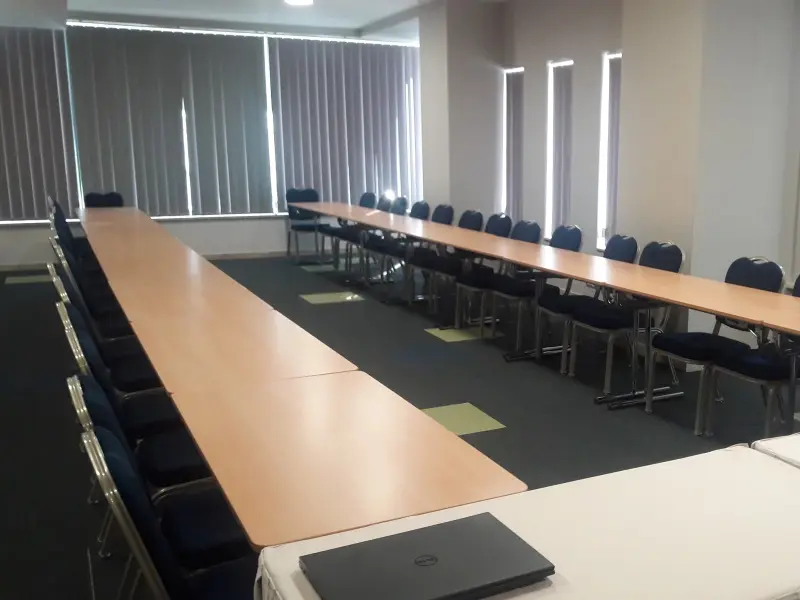 Konferencijska sala u Tre Canne hotelu sa stolovima u U-rasporedu, plavim stolicama, laptopom i vertikalnim roletama