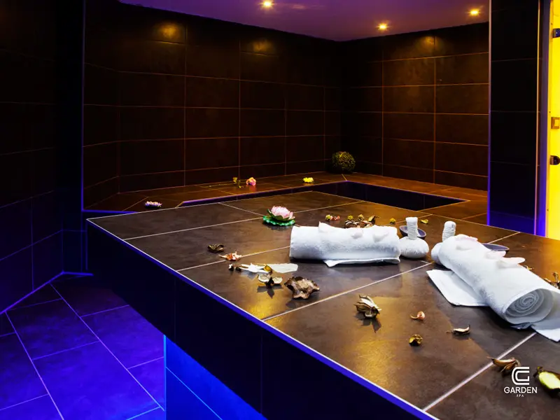 Hamam bazen u Garden Spa Boutique Hotel sa tamnim pločicama, belim peškirima, dekorativnim laticama i plavim ambijentalnim osvetljenjem