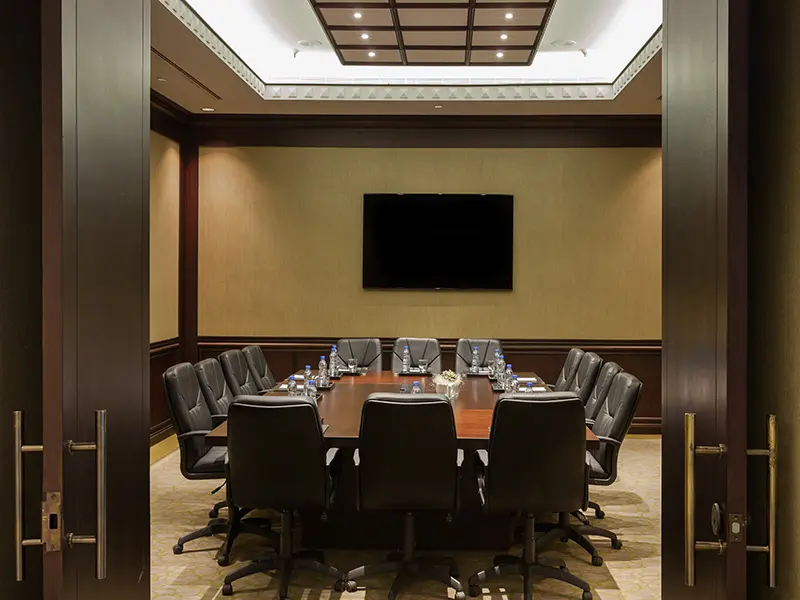 Klasična boardroom sala u Hyatt Regency Beograd sa tamnim drvenim stolom, crnim kožnim stolicama, TV ekranom i tamnim drvenim panelima