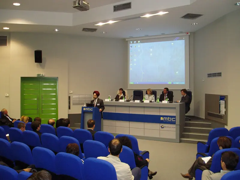 Auditorijum u ERA Group Skopje Fair Congress Center tokom predavanja sa MBC govorničkim pultom, projektorskim platnom, plavim foteljama i publikom