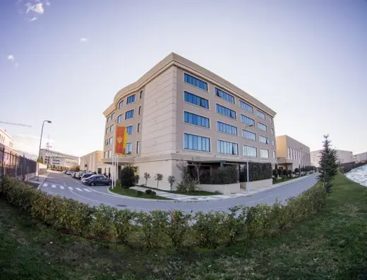 Panoramski pogled na fasadu Hotel voco Podgorica sa bež fasadom, zastavom Crne Gore, zelenim živicama, parkingom i plavim nebom