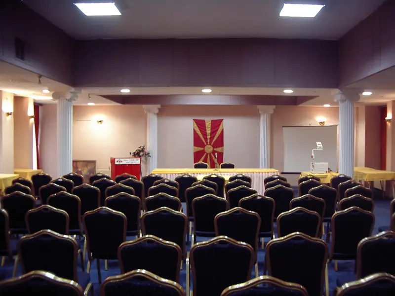 Konferencijska sala u Hotel Drim sa belim stubovima, crnim stolicama u teatarskom rasporedu, plavim tepihom i platnom za projekciju