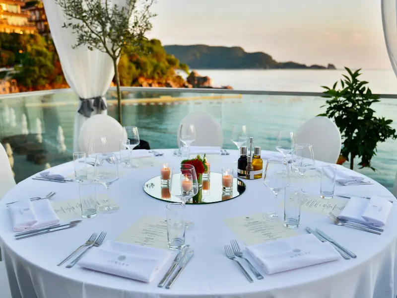 Banket sto na terasi Dukley Seafront Restaurant and Beach sa belim stolnjakom, svećama, Dukley menijem, belim zavesama i pogledom na more pri zalasku sunca