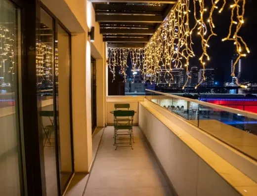 Balkon u Hotel Calisi noću sa dekorativnim lampicama, zelenim stolićem i pogledom na grad