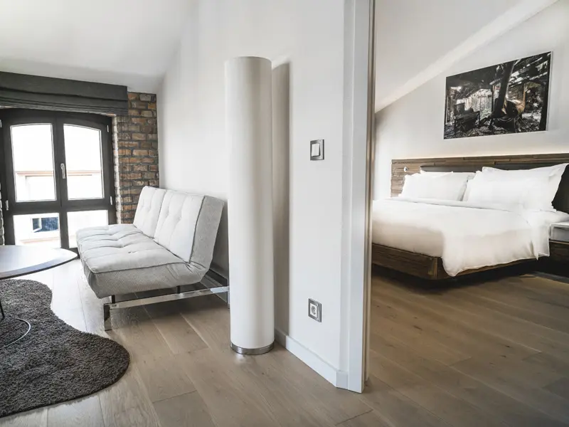 Apartman u hotelu Radisson Collection Hotel Old Mill Belgrade sa dnevnom sobom, sivim kaučem, ciglenim zidom, prozorima i spavaćom sobom vidljivom kroz pregradu