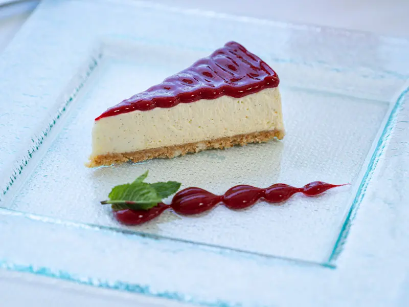Cheesecake sa sosom od maline na staklenom tanjiru u Dukley Seafront Restaurant and Beach sa listom nane i dekorativnim sosom