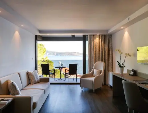 Dnevna soba apartmana u Palmon Bay Hotel & Spa sa sofom, foteljom, radnim stolom, TV-om, orhidejom i balkonom sa pogledom na more