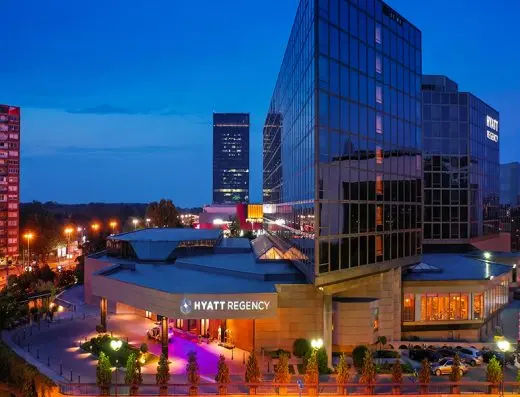 Noćni pogled na Hyatt Regency Beograd sa osvetljenom staklenom fasadom, ljubičastom rasvetom na ulazu i gradskim siluetom u pozadini