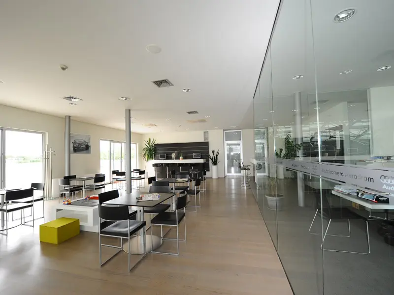 Lounge bar u Autokomerc Karting Centar sa crnim nameštajem, visokim barskim stolom, drvenim podom i staklenim zidovima sa pogledom na salon