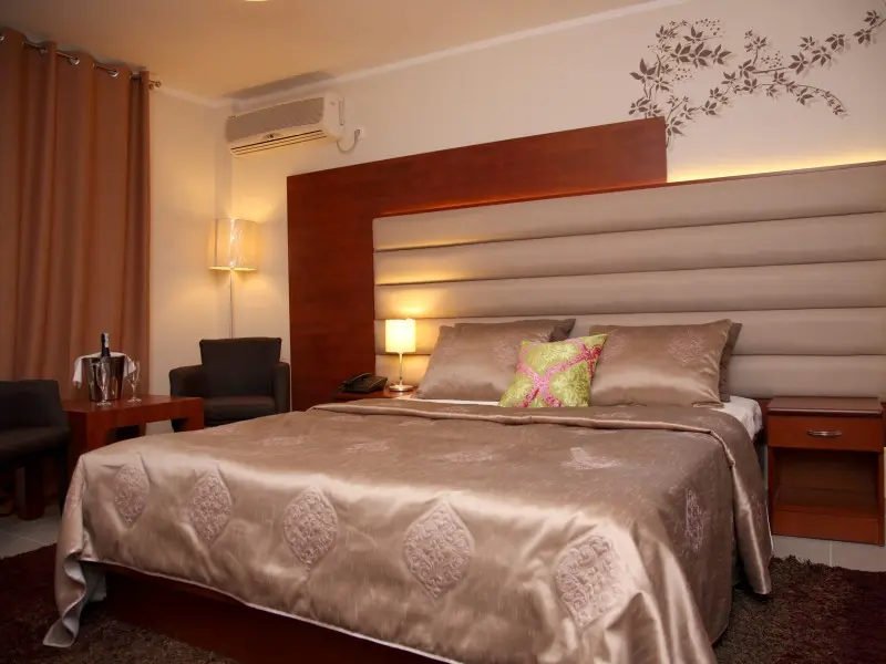 Soba sa bračnim krevetom u Hotel Mediteran Ulcinj sa satenskim prekrivačem u braon boji, drvenim uzglavljem sa LED osvetljenjem, foteljama i cvetnim dekoracijama na zidu