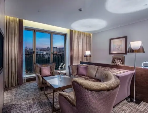 Dnevni boravak apartmana u Hilton Podgorica Crna Gora hotelu sa foteljom, kaučem, TV-om i večernjim pogledom na grad kroz balkonska vrata