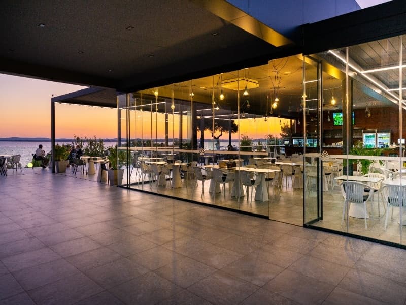Bar Hotel Pinija sa staklenom fasadom i terasom uz more tokom zalaska sunca