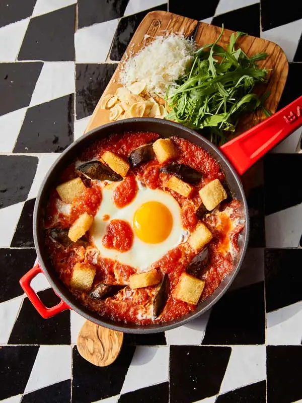 Jelo u Mama Shelter - shakshuka sa jajima u paradajz sosu, patlidžanom i krutonima u crvenom tiganju, sa rukolom i parmezanom na drvenoj dasci