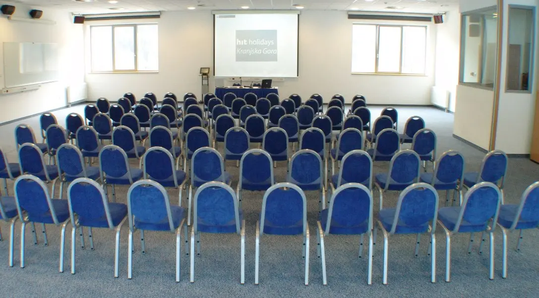 Konferencijska sala u Ramada Resort Kranjska Gora hotelu sa plavim stolicama u teatar rasporedu i projekcijom na platnu