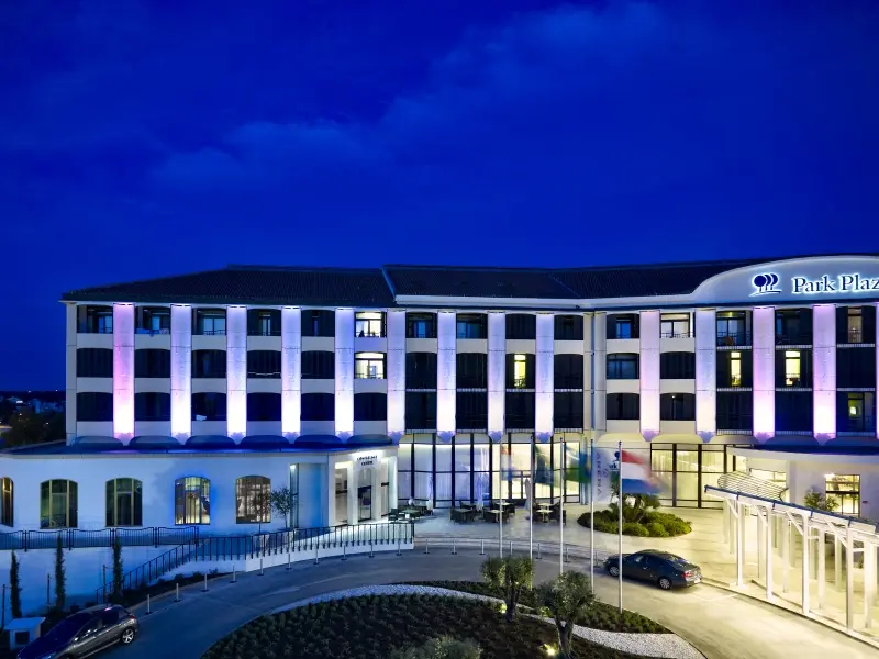 Eksterijer Hotel Park Plaza Histria Pula noću sa ljubičastim dekorativnim osvetljenjem fasade, natpisom Park Plaza i kružnim prilazom