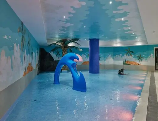 Dečji bazen u BOR Hotel by Karisma sa tobogom u obliku talasa, tropskim muralima na zidovima i plafonom sa oblacima