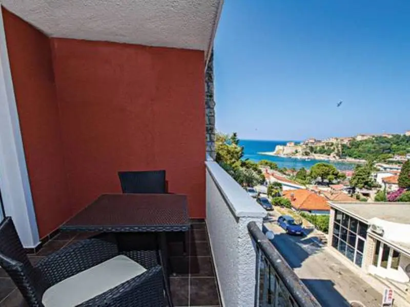 Balkon sobe u Hotel Mediteran Ulcinj sa ratanskim stolom i stolicama, crvenim zidom i panoramskim pogledom na Stari grad Ulcinj i more