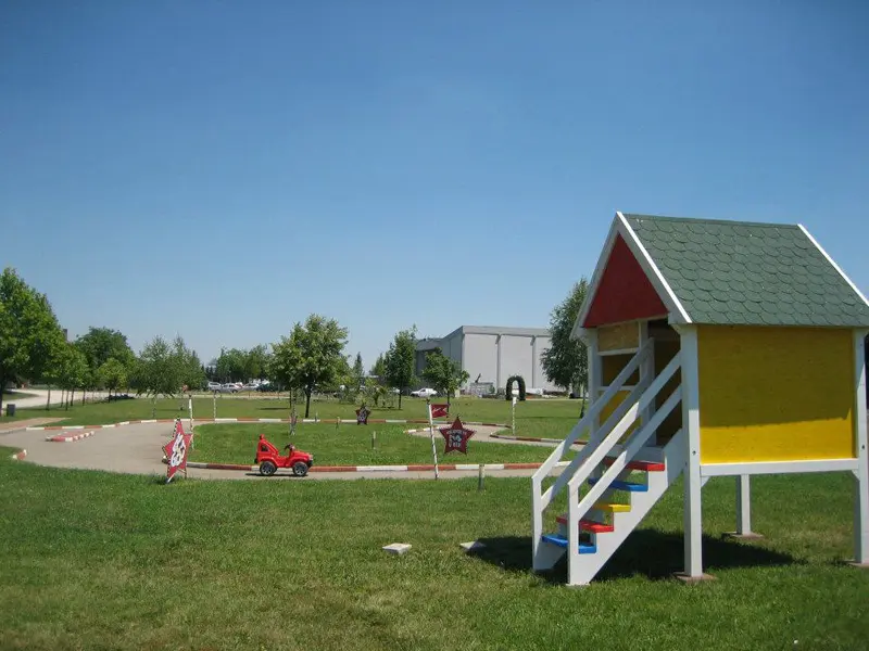 Dečije igralište u Autokomerc Karting Centar sa mini karting stazom, dečijim automobilom, drvenom kućicom i zelenim travnjakom