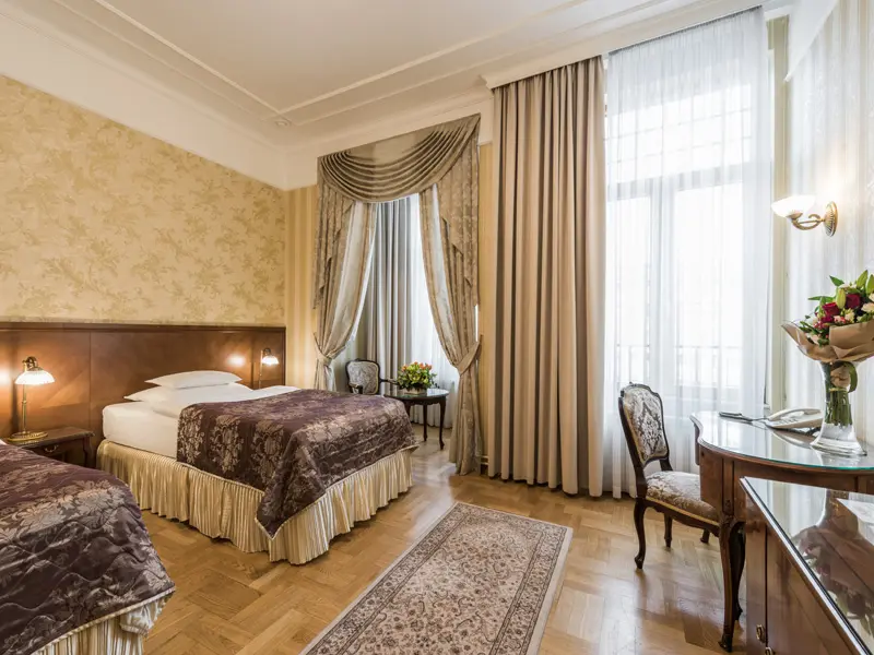 Soba sa dva kreveta u Hotel Moskva sa zlatnim zavesama, cvetnom tapetom, parketom i klasičnom foteljom
