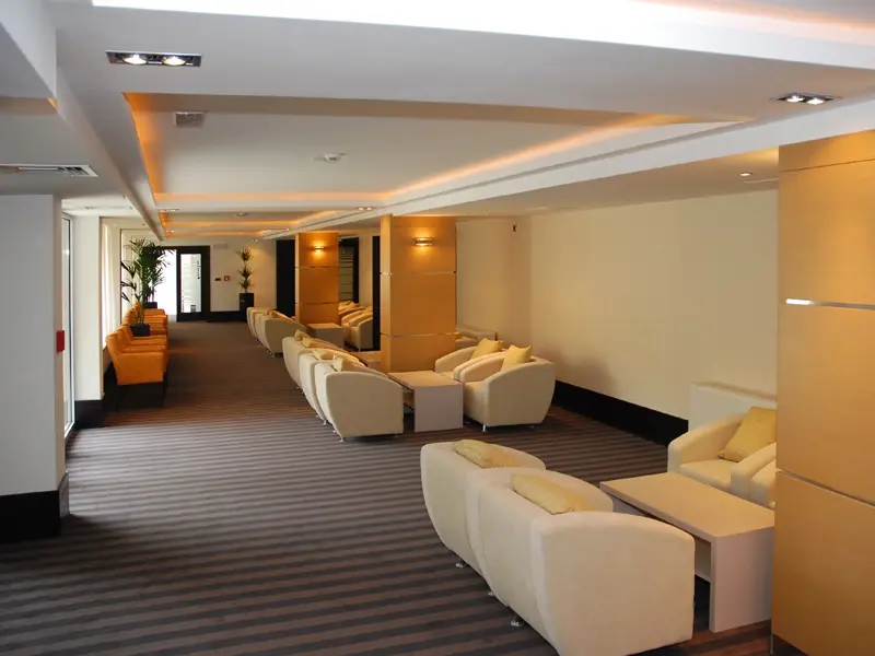 Hodnik lobija u Hotel Vojvodina sa belim foteljama, narandžastim akcentima, prugastim tepihom, drvenim zidnim panelima i indirektnim osvetljenjem