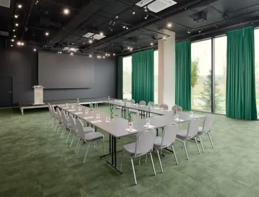 Konferencijska sala u Pullman Zagreb sa stolovima u U-rasporedu, sivim stolicama, zelenim tepihom, zelenim zavesama i binom sa govornicom
